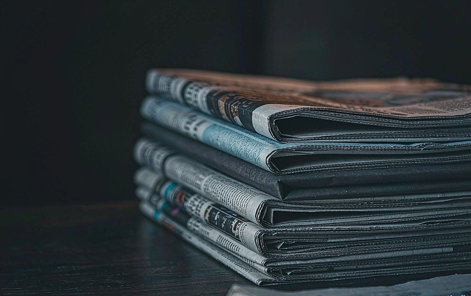 Stack of folded English newspapers on a dark editorial desk