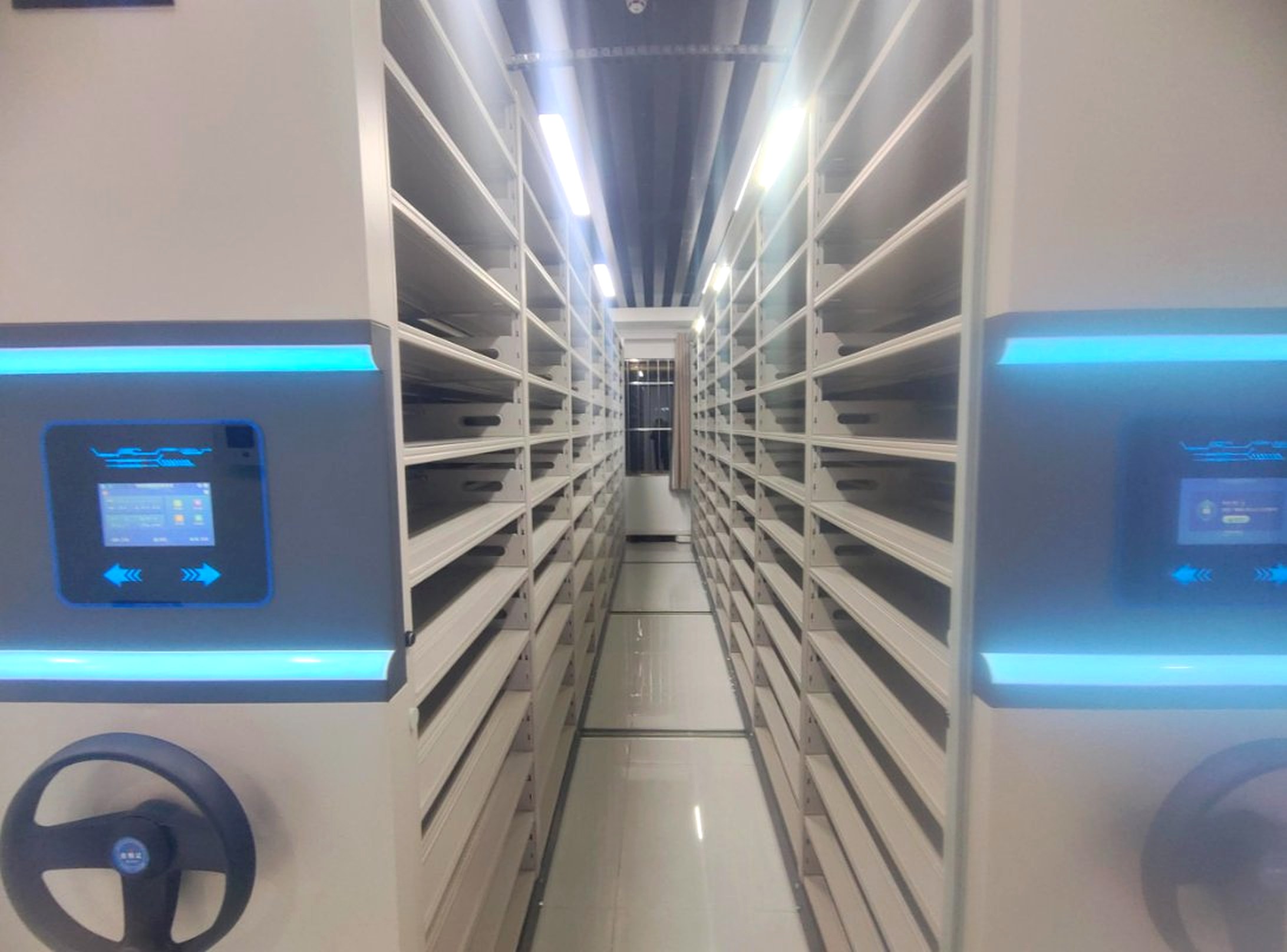 Aisle between voucher smart shelving bays with LCD terminals and hand wheels on both sides